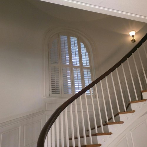 White plantation shutters decorating rounded window located in round stairwell.